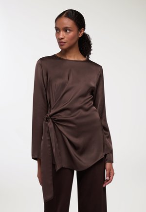 Top in satin marrone con dettaglio di nodo intrecciato in vita, maniche lunghe e scollo rotondo. Texture liscia e drappeggio fluido.