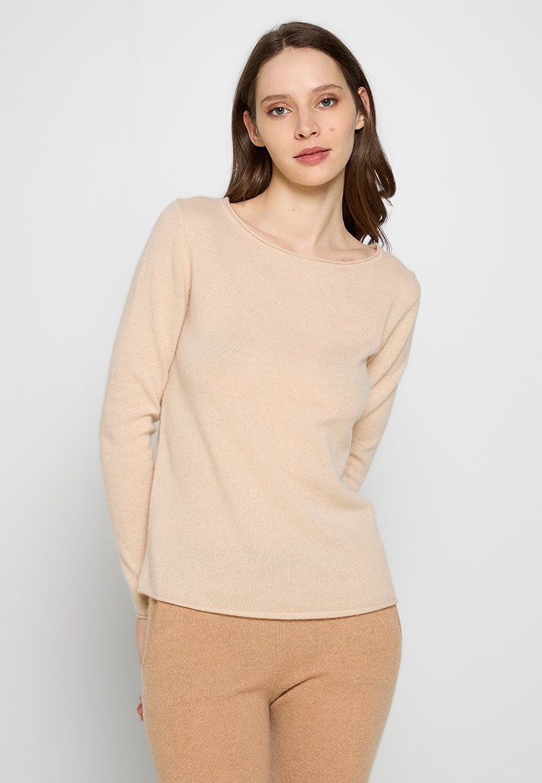 Beiger, langärmliger Pullover aus weichem Strickstoff mit weit geschnittenem Rundhalsausschnitt; glatte Textur, figurbetonter Schnitt, kombiniert mit beigen Leggings.