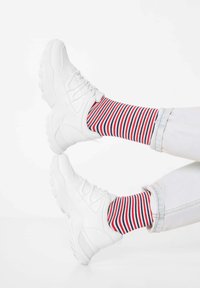 Weiße Sportschuhe mit strukturierten Sohlen und Schnürsenkeln, kombiniert mit mehrfarbigen gestreiften Socken in Rot, Weiß und Blau.
