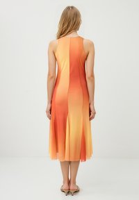 Vue arrière d'une robe sans manches affichant un dégradé de couleurs orange et jaune, fabriquée dans un tissu léger avec un ourlet évasé.