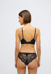 Crni grudnjak od čipke i gaćice koje se slažu, s cvjetnim uzorcima, podesivim trakama i kopčanjem na kuke i očice na grudnjaku.