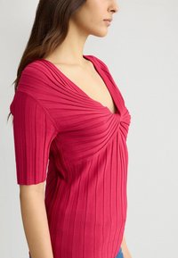 Top ajustat cu dungi în roz aprins, cu decolteu adânc în V, având detalii elegante plisate și mâneci scurte, realizat dintr-un material moale și elastic.