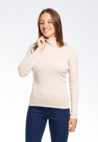 Maglione a collo alto beige in una vestibilità aderente con maniche lunghe, realizzato in un tessuto liscio. Indossato con jeans in denim scuro.