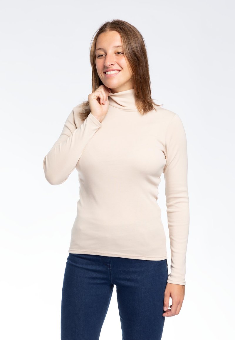 Maglione a collo alto beige in una vestibilità aderente con maniche lunghe, realizzato in un tessuto liscio. Indossato con jeans in denim scuro.