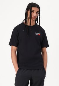 T-shirt noir à manches courtes en coton, avec un petit logo rouge et blanc sur la poitrine. Coupe droite avec une coupe décontractée.