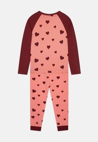 Lange mouwen pyjama set in zachtroze met bordeauxrode accenten, met een hartjespatroon. Geribde manchetten op de mouwen en broek.