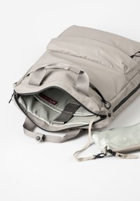 Lichtgrijze rugzak met een gevoerde buitenkant, een geventileerd hoofdvak, interne vakken en een afneembare groene pouch. Gladde, waterdichte materialen.