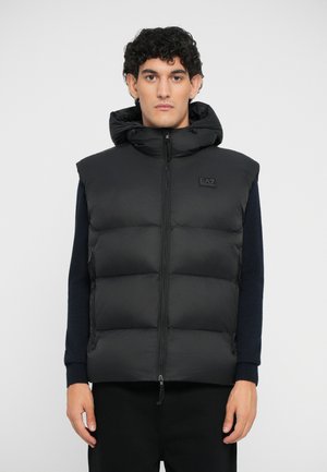 Black puffer vest with a hood, featuring a zip front, side pockets, and a logo patch on the chest. Smooth texture and padded sections.