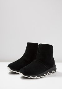 Melni zamšīgi potīšu zābaki ar teksturētu melnu gumijas zoli. Iespējas ietver zemu profilu, noapaļotu purngalu un sānu rāvējslēdzēju vieglai uzvilkšanai.