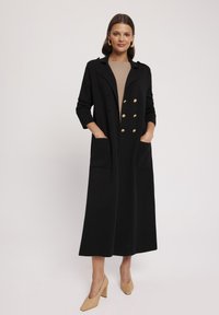 Czarny podwójnie zapinany płaszcz z złotymi guzikami, długimi rękawami i kieszeniami bocznymi, charakteryzujący się eleganckim krojem i gładką fakturą tkaniny.