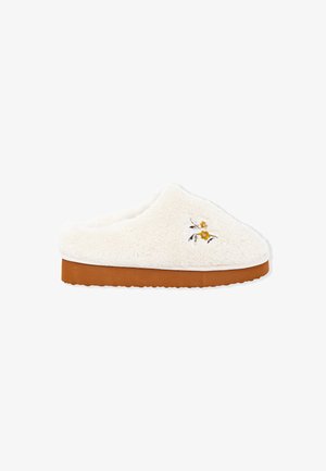 Chausson moelleux de couleur crème avec une semelle brune et de petites fleurs jaunes et blanches brodées sur le dessus.