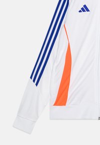 Weißer Sportjackenärmel mit blauen Adidas-Streifen, orangefarbenem Seitenbereich und blauem Adidas-Logo auf der Brust.
