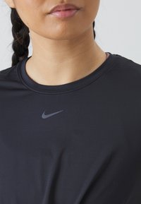 Fekete sportpóló kerek nyakkivágással és rövid ujjakkal. A felső mellkason egy kis szürke Nike logó található. Sima textúra.