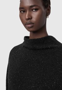 Schwarzer Pullover mit strukturierter Optik, ausgestattet mit einem hohen Kragen und gepunktetem Muster. Der Stoff erscheint weich und hat ein gemütliches Design.