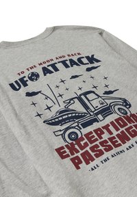 T-shirt in cotone grigio con un design grafico di un camion e un UFO. Il testo include "ATTACCO UFO" e "PASSEGGERI ECCEZIONALI" in blu scuro e rosso.
