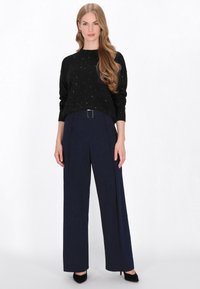 Sort striktrøje med sølvprikker, parret med marineblå vide bukser med bælte og en glat tekstur. Sorte hæle fuldender looket.