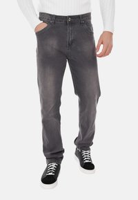 Jeans in denim grigio scuro con una finitura sbiadita, dotati di cinque tasche, chiusura con bottone e gamba dritta. Indossati con sneakers nere.