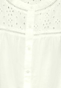 Vit blus med delikat broderi och utskärningar vid axelpartiet, framknappringning och mjukt, texturerat tyg.