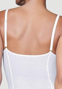 Body bianco con spalline sottili, caratterizzato da una superficie liscia e una discreta brandizzazione, che mette in mostra un design pulito e minimalista.