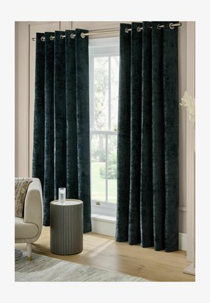 Dunkelblaue Samtvorhänge mit Metallösen hängen offen an einem Fenster neben einem beigen Sofa und einem runden Beistelltisch mit einem Glas Wasser.