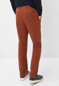 Mørkeorange bomuldsbukser med en slim fit, der har baglommer, diskret branding og en glat tekstur, parret med mørke sneakers.