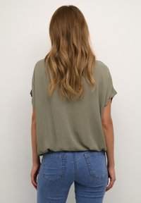 Top de manga corta en verde oliva con un corte relajado, combinado con jeans azules que presentan un diseño clásico de cinco bolsillos y detalles de costura sutiles.