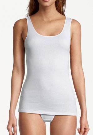 Frau trägt ein eng anliegendes weißes ärmelloses Tanktop und passende weiße Unterwäsche vor einem schlichten hellen Hintergrund.