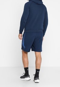 Felpa navy con cappuccio e coulisse, abbinata a pantaloni corti navy con dettagli blu e tessuto leggero.