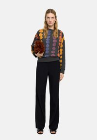 Bluza z grafiką z okrągłymi wielokolorowymi kropkami, ciemnoszara baza, ściągacze na rękawach, zestawiona z czarnymi szerokimi spodniami i czarnymi sandałami.