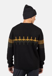 Czarny sweter z okrągłym dekoltem, zdobiony geometrycznym wzorem w żółtym, zielonym i szarym kolorze na plecach. Widoczna dzianinowa tekstura oraz długie rękawy.