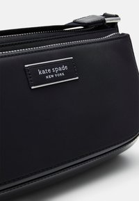 Borsa a tracolla nera in nylon con dettagli in pelle lucida, chiusura con zip e una placca con logo argentato sul davanti. Texture liscia, forma arrotondata.