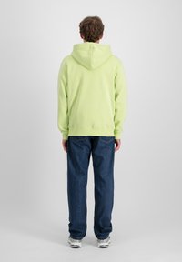 Sudadera con capucha de color verde claro, fabricada en material suave, combinada con jeans de corte holgado de color azul oscuro. Diseño sencillo, sin patrones ni acentos visibles.