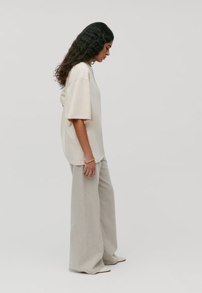 Beżowy, oversize T-shirt z krótkimi rękawami i okrągłym dekoltem, zestawiony z jasnoszarymi spodniami z szerokimi nogawkami, wykonanymi z teksturowanej tkaniny.
