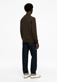 Brauner Pullover mit langen Ärmeln, gerippten Bündchen und Saum, kombiniert mit dunkelblauen Jeans und weißen Sneakers mit beigen Sohlen.