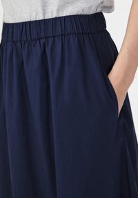 TMavě modrá, lehká sukně z látky s elastickým pasem a bočními kapsami. Hladká textura, jednoduchý design.