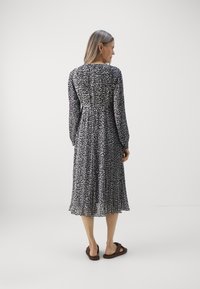 Pitkähihainen musta-valkoinen kuviollinen mekko, jossa on laskoksia, pitkä hihainen ja vyötäisille istuva malli. Yhdistetty tummiin sandaaleihin. Sujuvaa, kevyttä kangasta.