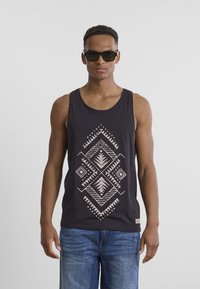 Black tank top with a geometric cream pattern, featuring a rounded neckline. Model wearing dark sunglasses and blue jeans.