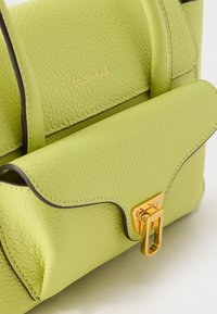 Τσάντα χειρός από δέρμα με ανοιχτό πράσινο χρώμα και υφή, με χρυσό κούμπωμα και εγχάρακτο το λογότυπο "COCCINELLE" στην εμπρόσθια πτέρυγα, διαθέτει διπλές λαβές και σκουρόχρωμες περιμετρικές άκρες.