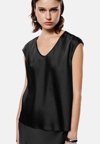 Top in satin nero con scollatura a V, maniche a palloncino, vestibilità ampia e texture liscia. Progettato con accenti minimi e una leggera lucentezza.