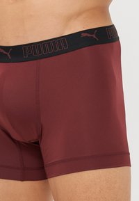 Boxeri maronii dintr-un material neted, cu un brâu elastic negru ce prezintă logo-ul "PUMA" în litere roșii.