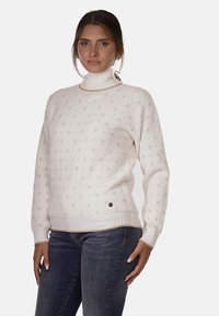 Maglione bianco a maglia con collo alto, caratterizzato da un leggero motivo a rombi e polsini e orlo a costine. Dettaglio a bottoni in basso a sinistra.