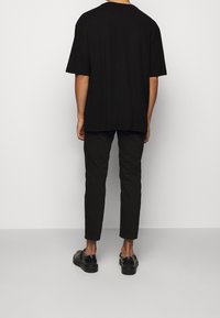 Black oversized t-shirt with short sleeves, paired with dark slim-fit trousers and black shoes. The fabric appears smooth with a relaxed fit.