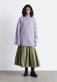 Oversized lilac turtleneck sweater made of soft fabric, paired with a flowy olive-green skirt and black lace-up platform boots.