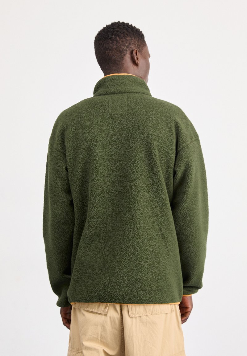 Groene fleece pullover met een hoge kraag, met een gestructureerd oppervlak en een oranje accent aan de zoom. Ontworpen voor warmte en comfort.
