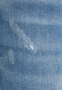 Tecido de denim azul claro com uma superfície texturizada. Apresenta dois remendos desbotados e padrões de trama diagonal subtis.