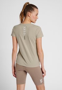 Khakifarbenes T-Shirt mit kurzen Ärmeln und rundem Halsausschnitt, auf der Rückseite mit einem vertikalen Streifendesign in Weiß; kombiniert mit braunen Shorts.
