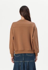 Bruine oversized sweatshirt met een ronde hals en ribboorden, met een soepele textuur en subtiele stiksels aan de achterkant.
