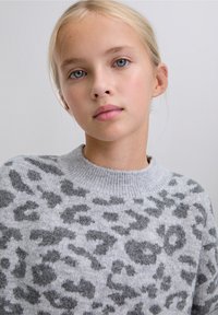 Suéter gris con una textura suave y manchas de leopardo en un gris más oscuro, con un cuello acanalado. El diseño es casual y de corte relajado.