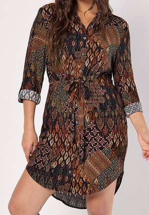 Robe chemise à boutons en tissu foncé avec des motifs multicolores complexes. Taille nouée, manches trois-quarts avec poignets à motifs, et légère fronces.