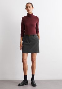 Burgundy polokrage topp, grå kjol med fickor, svart bälte, mörka strumpor och svarta loafers. Slätt tyg och skräddarsydd design.